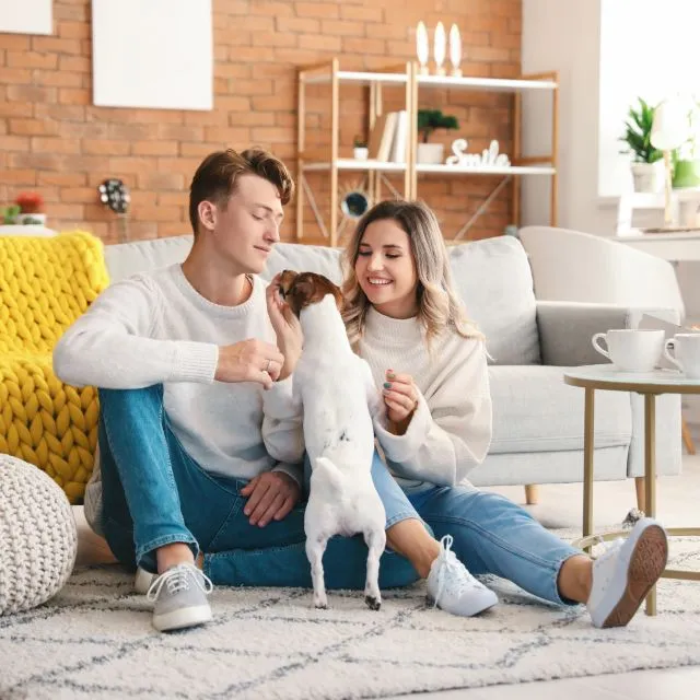 A young couple plays with their dog on the living room rug